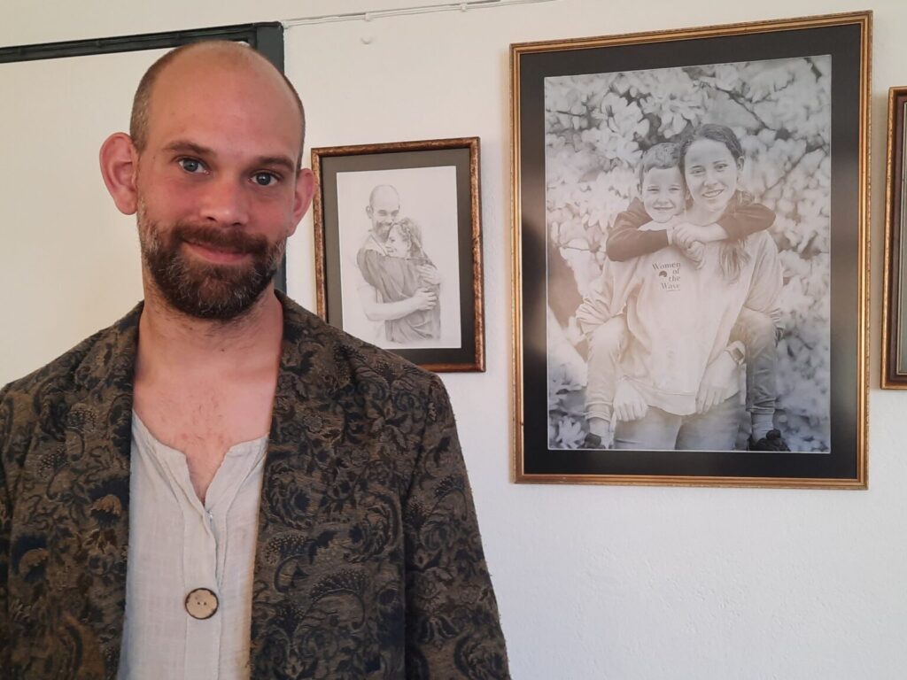 Hilbert van der Staal standing next to his hyper realistic pencil drawing portraits.
